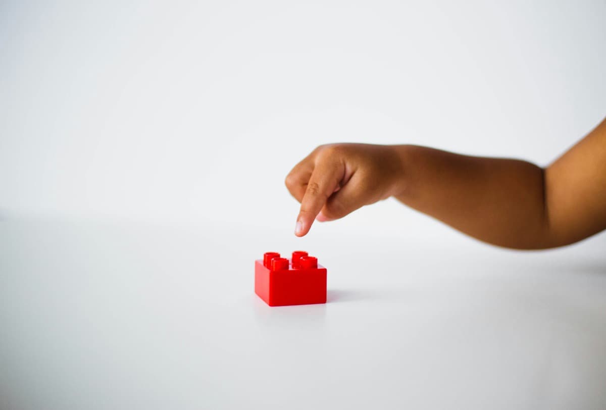 A child's hand reaching for a red building block